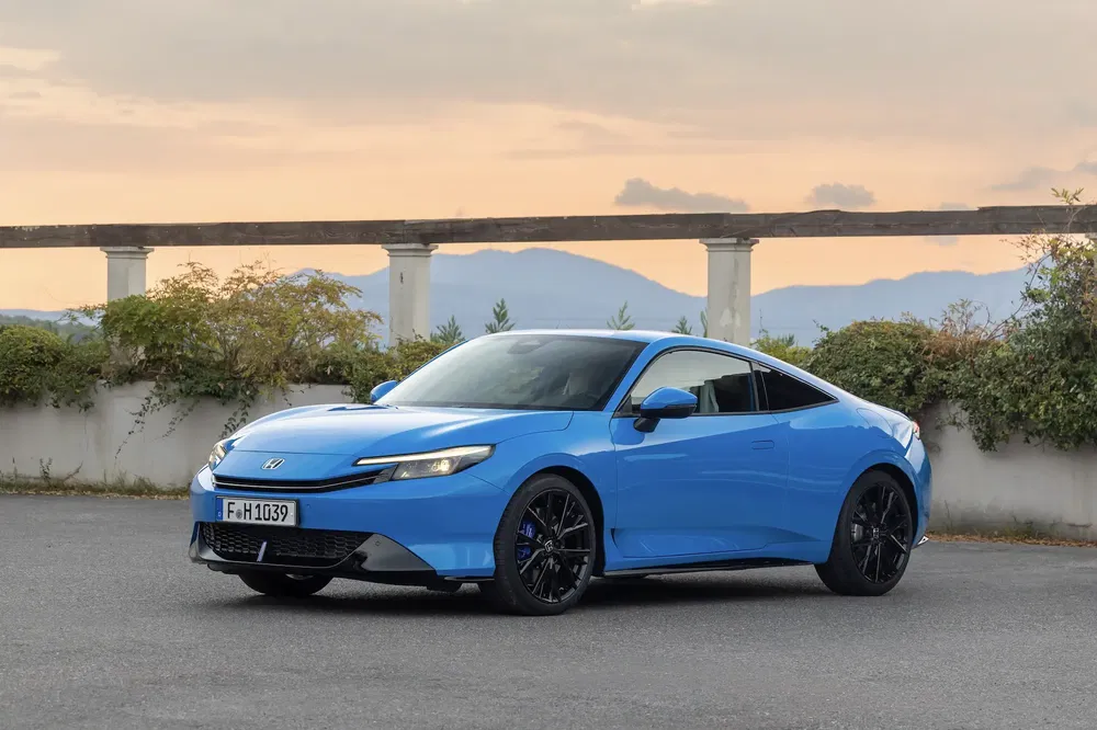 Blauwe Honda Civic coupé geparkeerd voor een schilderachtige zonsondergang op de achtergrond.