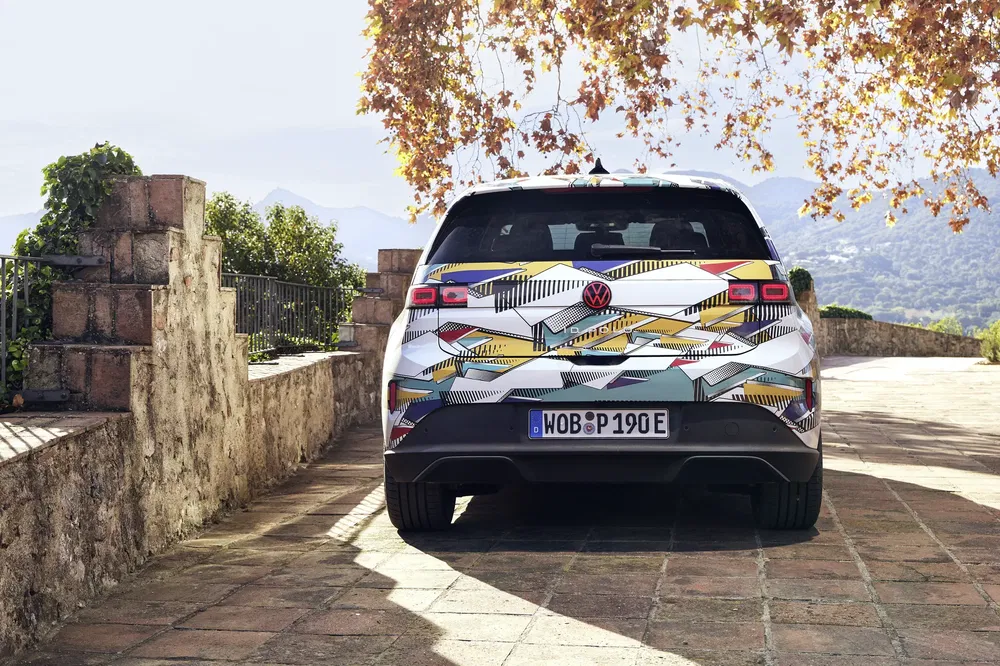 Volkswagen ID. Buzz camouflée stationne sous des arbres aux feuilles automnales.