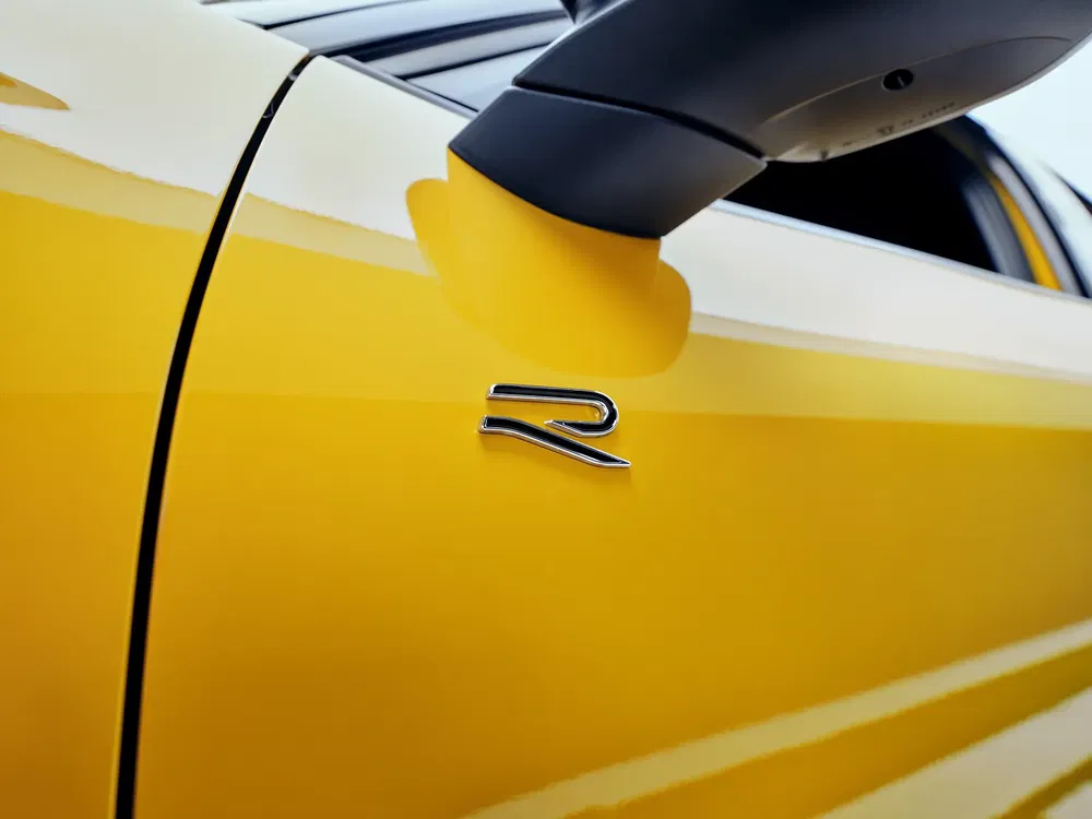 Volkswagen R-logo op gele auto met zwarte zijspiegel.