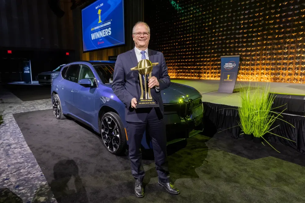 Man met trofee voor een blauwe BMW iX bij een prijsuitreikingsevenement.