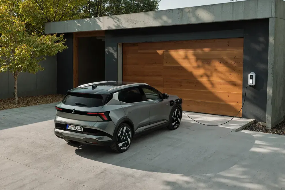 SUV électrique Mitsubishi Outlander gris chargeant devant une maison moderne.