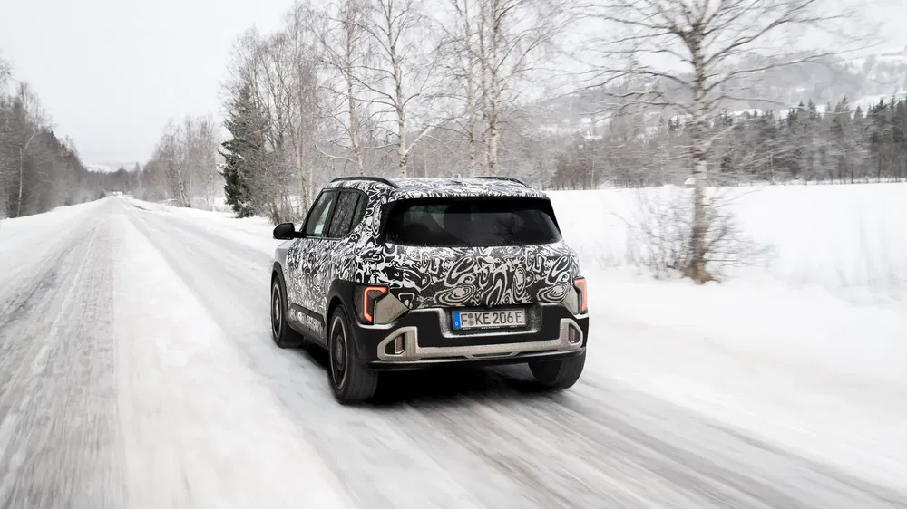 SUV camouflé BMW iX1 roulant sur route enneigée bordée d'arbres hivernaux.