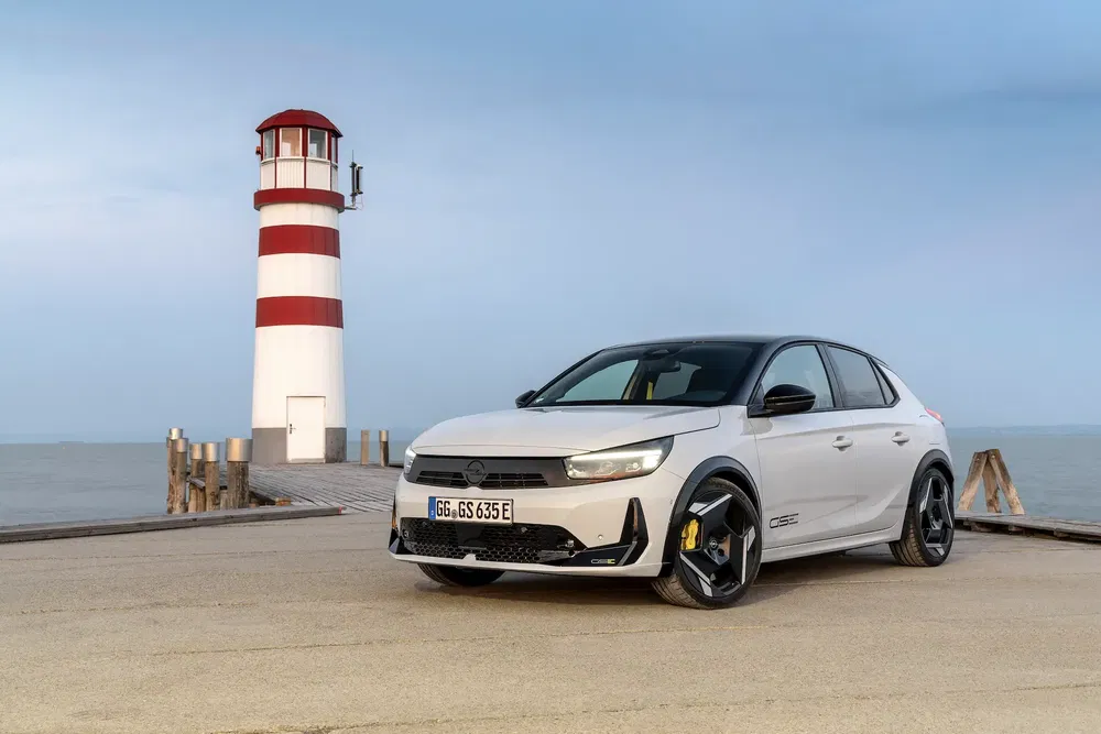 Opel Astra blanche devant un phare au bord de la mer, mise en valeur au coucher de soleil.