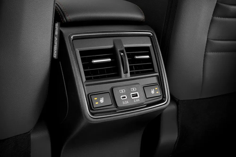 Achter airconditioningsopeningen met USB-poorten en stoelverwarmingsbediening in een auto.