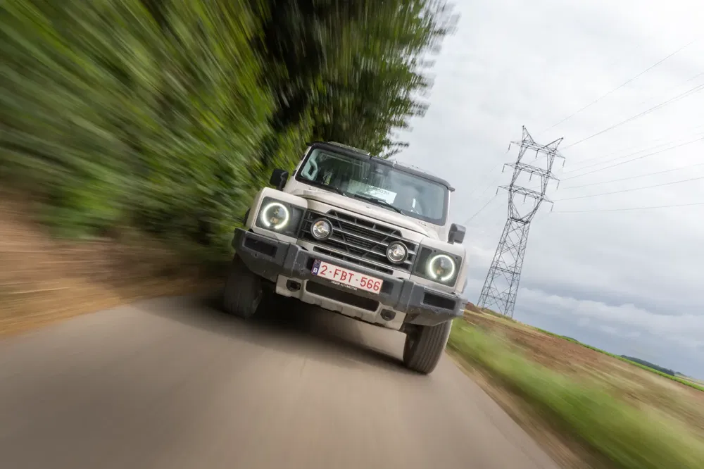 Witte Mercedes-Benz G-Klasse 4x4 rijdt op een landweg met bomen.