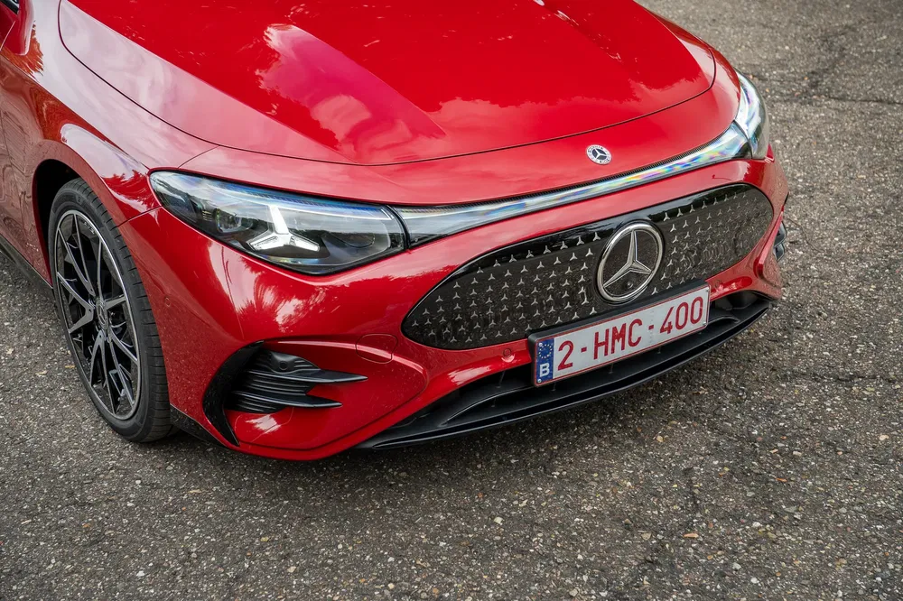 Close-up van een rode Mercedes op stedelijke weg, met opvallende grille in focus.