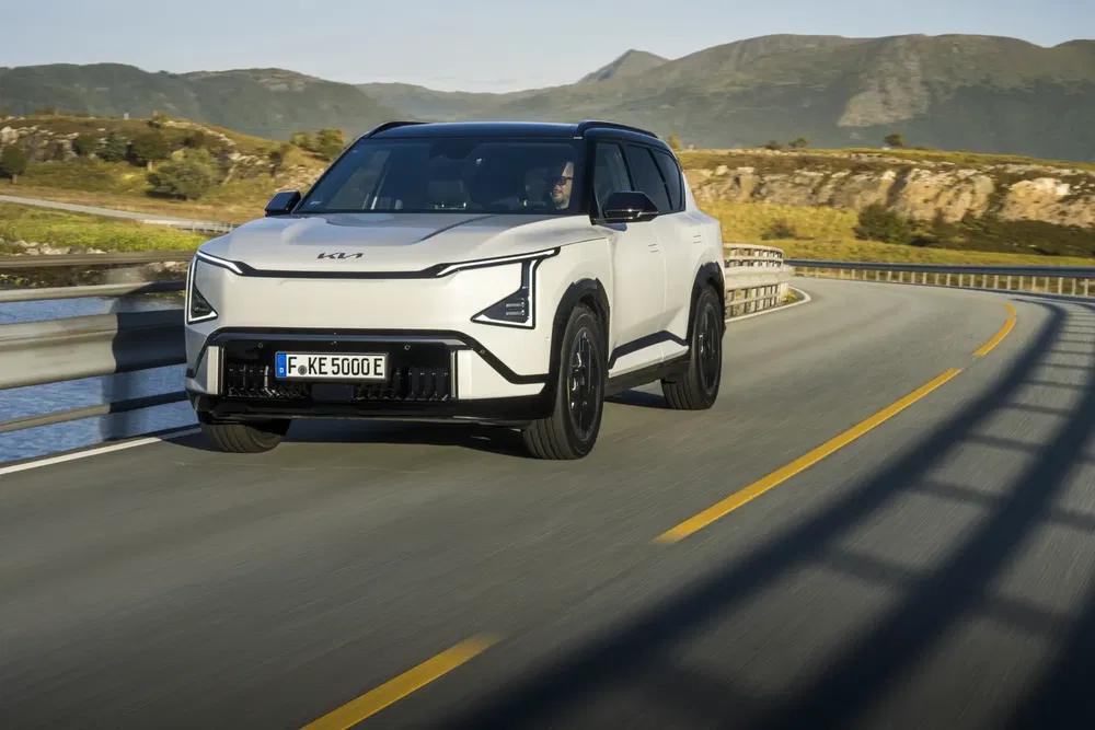 Kia EV9 blanc roulant sur une route sinueuse avec des montagnes en arrière-plan.