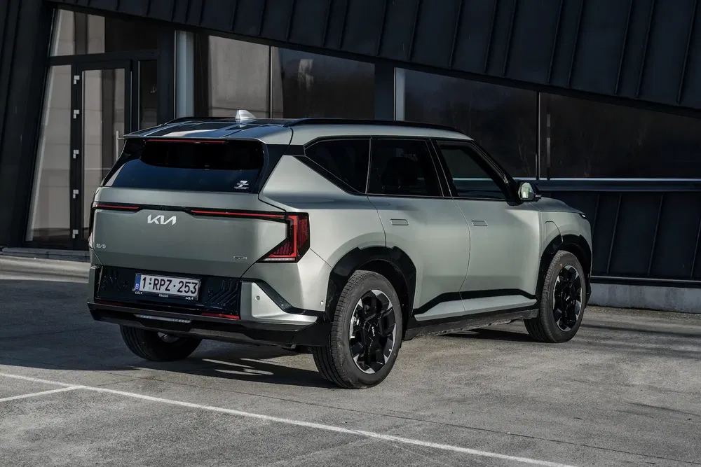 Kia EV9 gris stationné devant un bâtiment moderne, vue arrière audacieuse et angulaire.