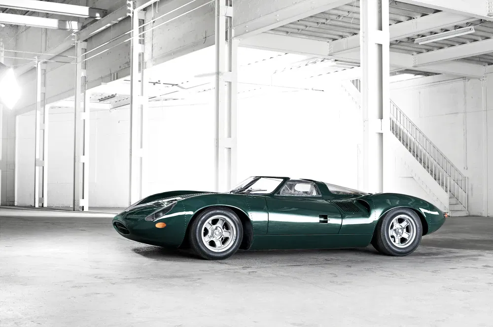 Voiture classique Jaguar XKSS verte dans un entrepôt industriel spacieux et lumineux.