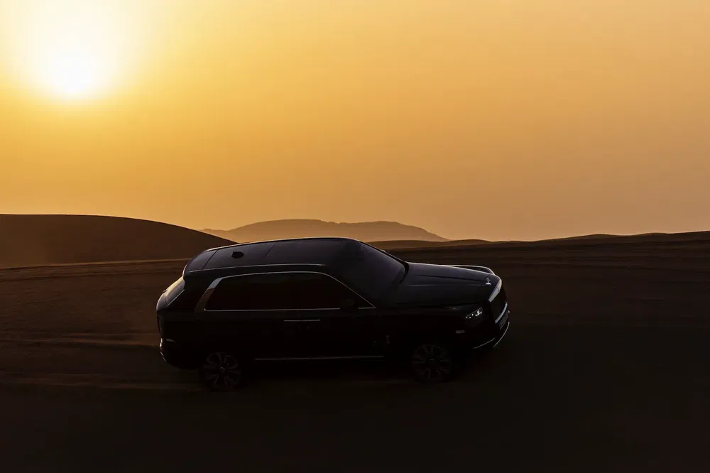 SUV luxueux Rolls-Royce Cullinan silhouette au coucher du soleil sur dunes de sable.