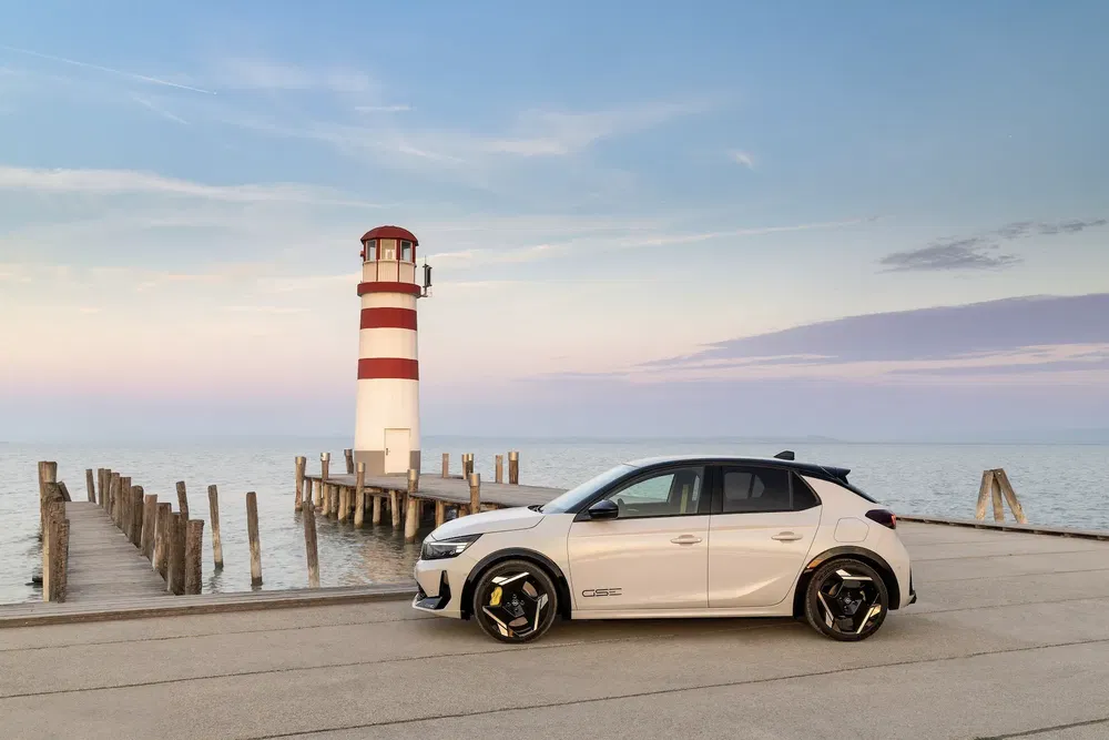 Opel Astra GSe blanche près d'un phare rouge et blanc au bord de l'eau.