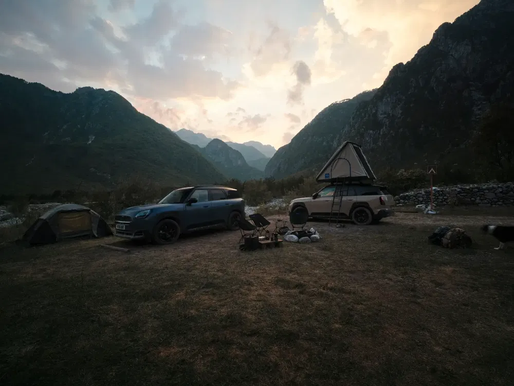 Paysage de montagne avec voitures Mini et SUV équipées de tentes de toit au coucher du soleil.