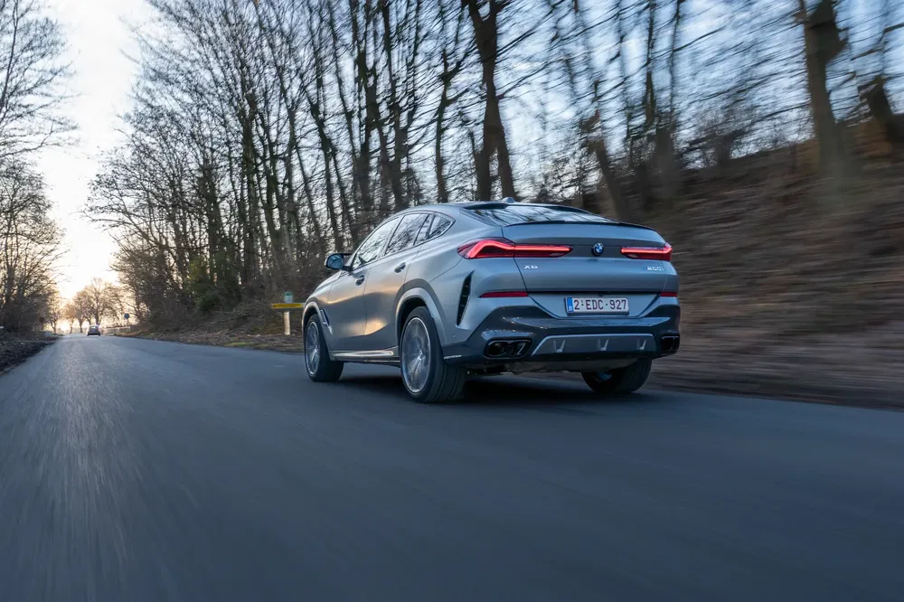 BMW X6 roulant sur une route de campagne bordée d'arbres en hiver.