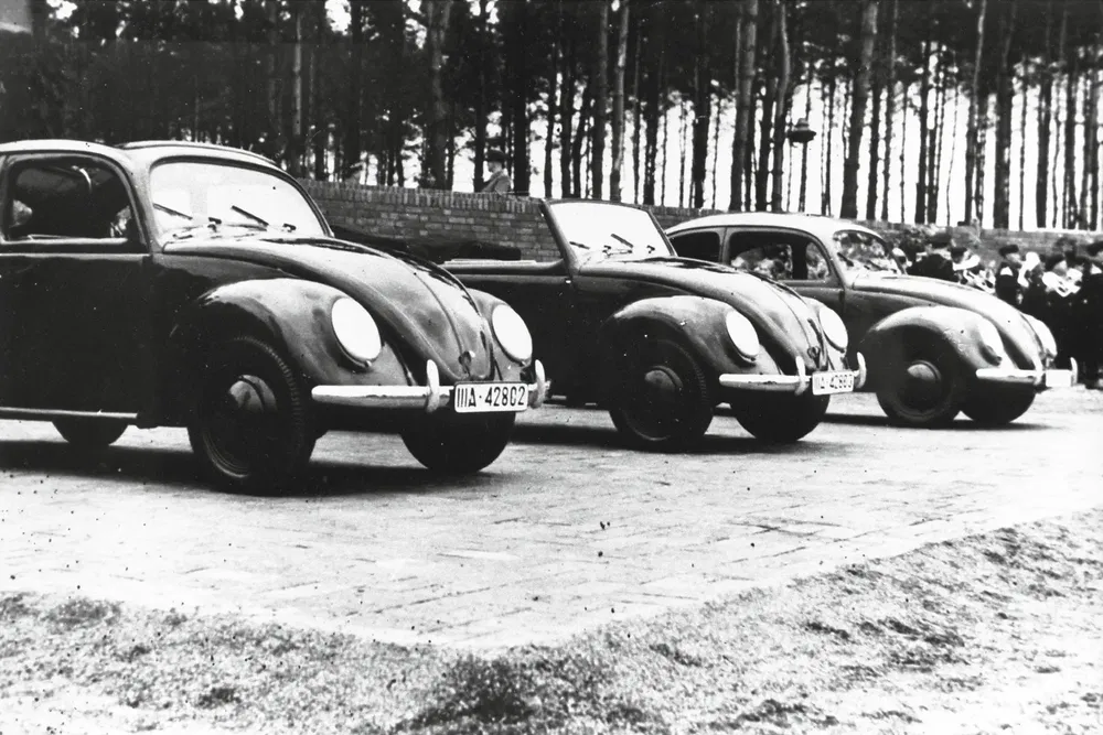 Trois Volkswagen Coccinelle anciennes alignées, forêt en arrière-plan.