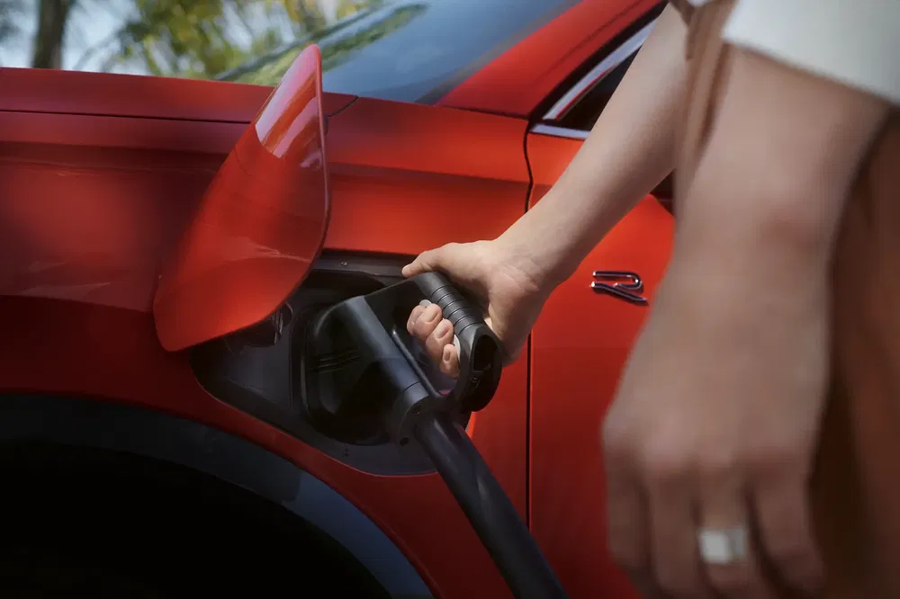 Recharge d'une voiture électrique rouge avec un câble de charge à proximité d'un bosquet.