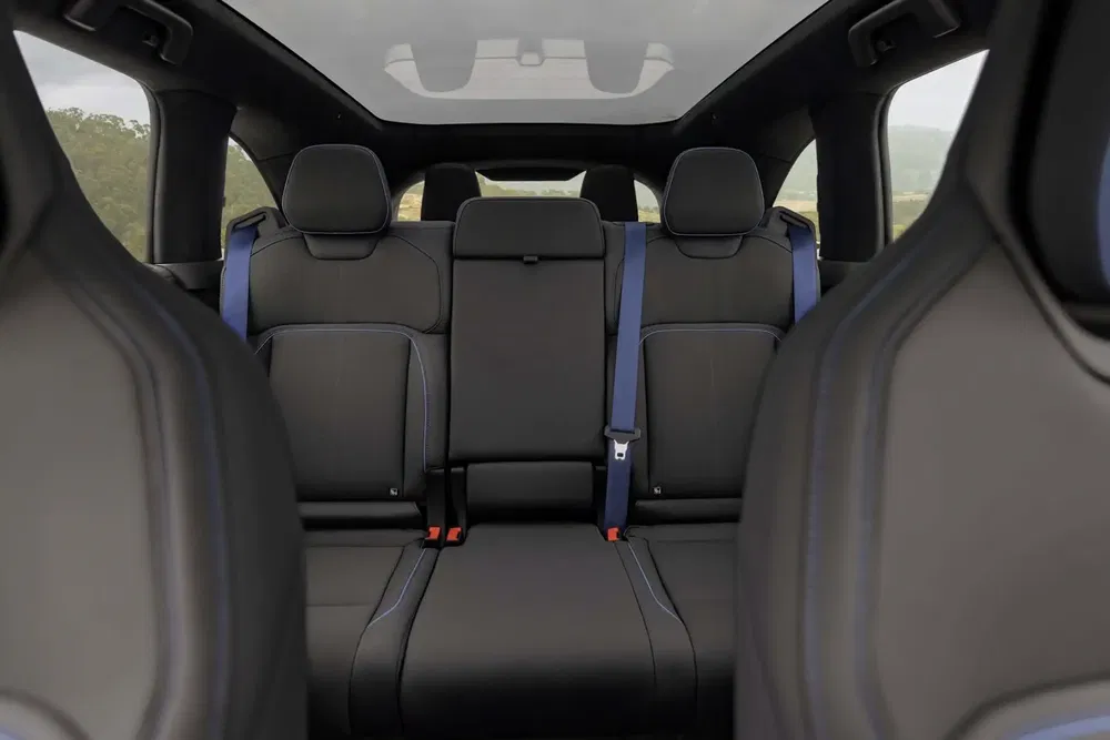 Ruim interieur van een Tesla Model X met zwarte lederen stoelen en blauwe gordels.