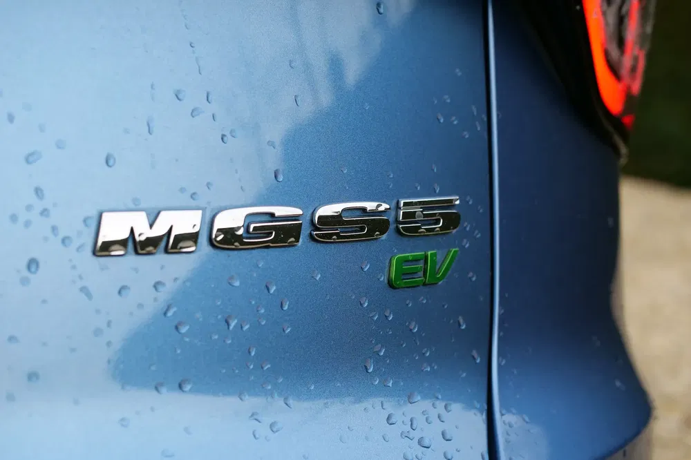 Insigne arrière MG5 EV sur carrosserie bleue, avec gouttes d'eau visibles.