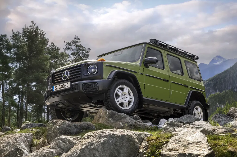 Groene Mercedes-Benz G-Klasse terreinwagen op rotsen met bergachtige achtergrond.
