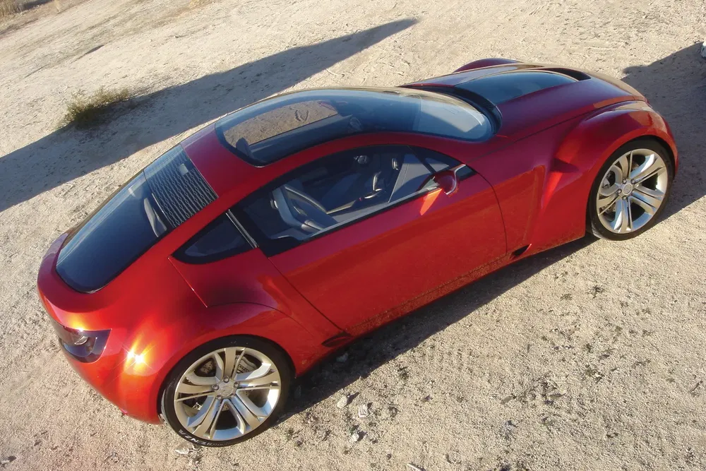 Voiture concept rouge avec toit vitré sur terrain désertique.