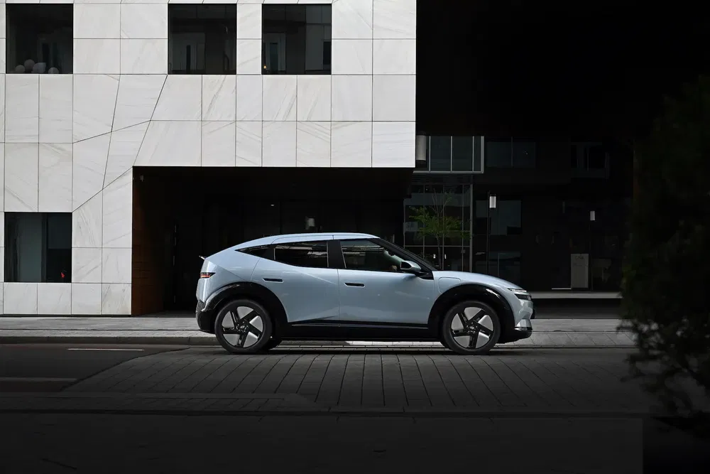 Profil d'une Kia EV6 blanche garée devant un bâtiment moderne en pierre.