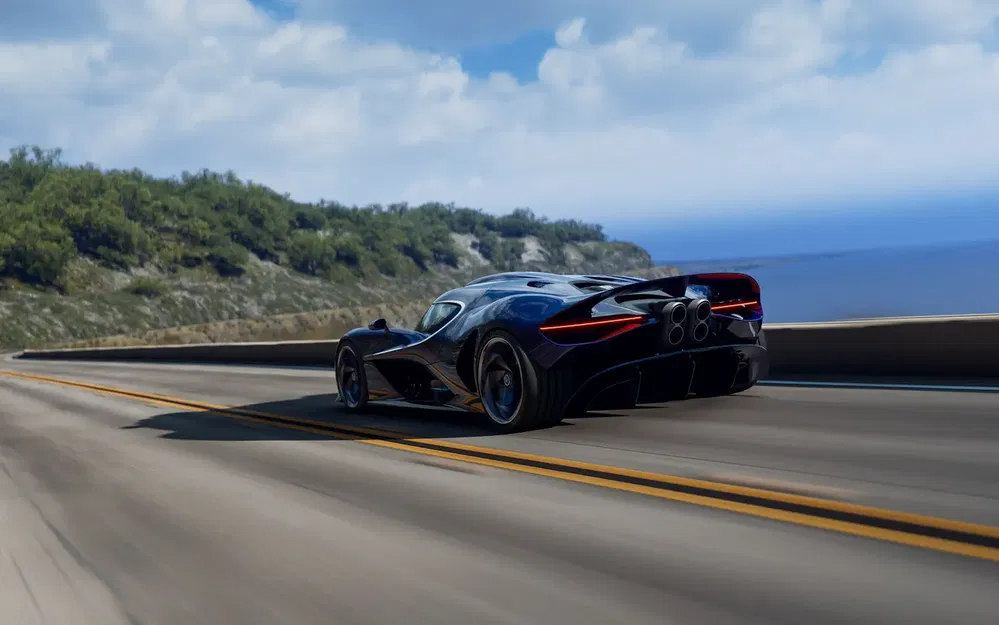 Zwarte hypercar op kronkelige kustweg met uitzicht op de oceaan en blauwe lucht.