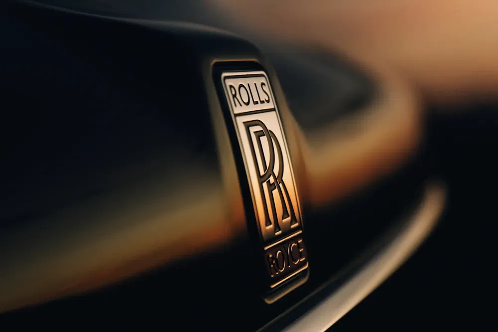 Gros plan du logo Rolls-Royce sur le capot d'une voiture au coucher du soleil.
