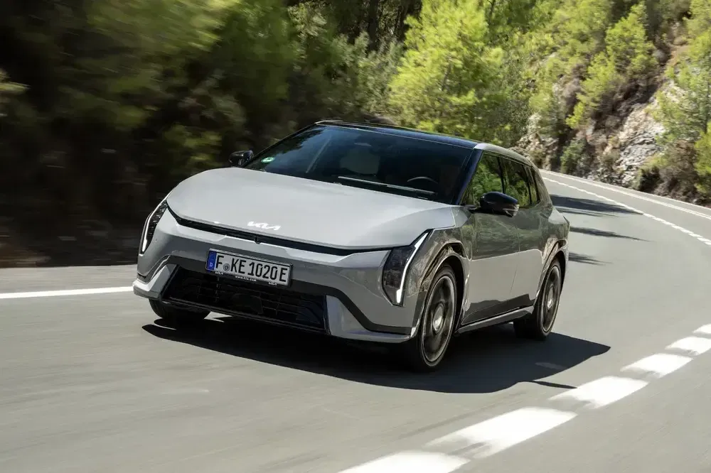 Kia EV9 grise roulant sur une route de montagne bordée d'arbres verdoyants.