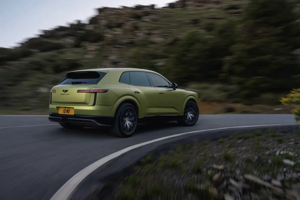 Bentley Bentayga verte sur une route sinueuse de montagne, arrière dynamique en mouvement.