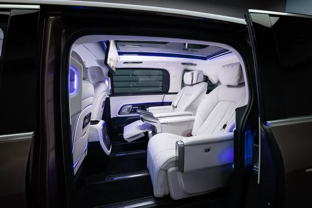 Luxe interieur van een bestelwagen met witte leren stoelen en stijlvolle LED-verlichting.
