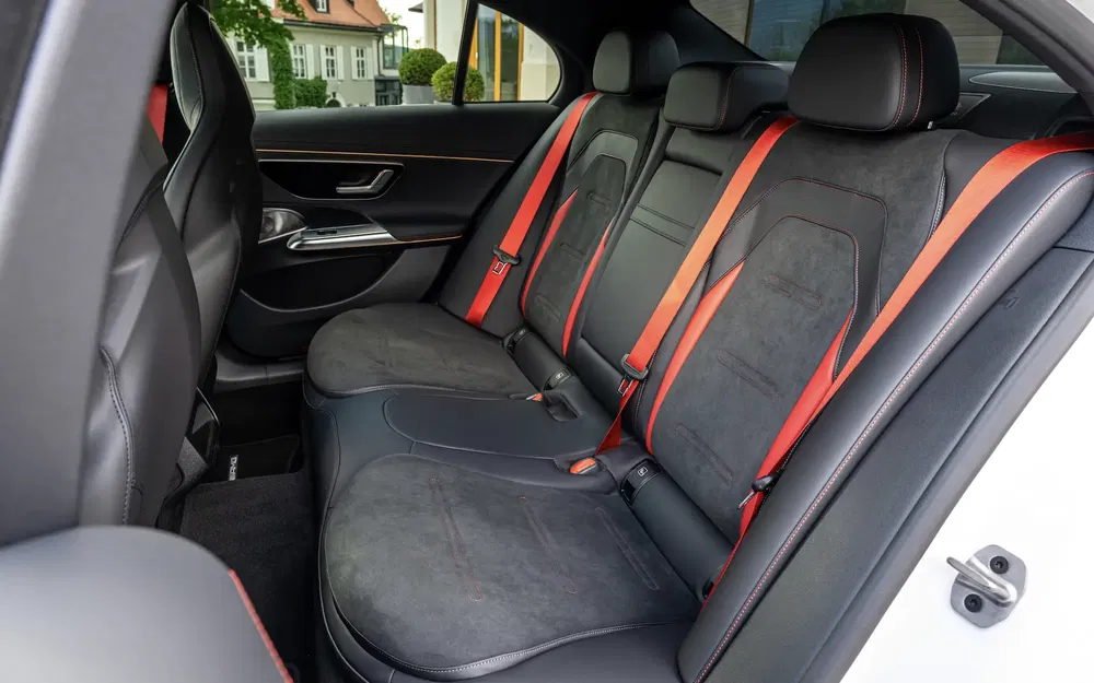 Intérieur arrière d'une voiture avec sièges en cuir noir et ceintures de sécurité rouges.
