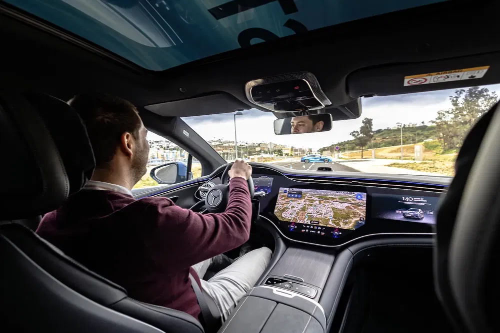 Bestuurder in een moderne Mercedes EQS met digitaal dashboard.