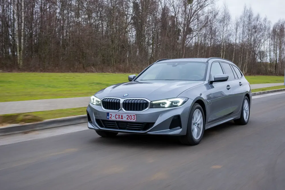 BMW Série 3 Touring roule sur une route, fond boisé, ciel nuageux.