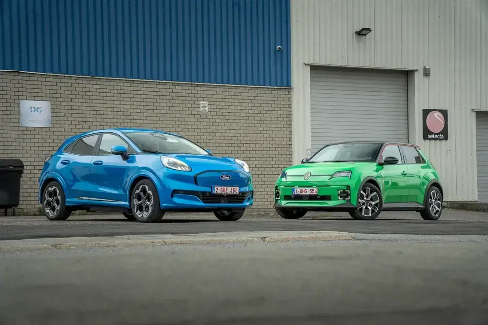 Twee auto's, Ford in blauw en Renault in groen, geparkeerd voor een industrieel gebouw.