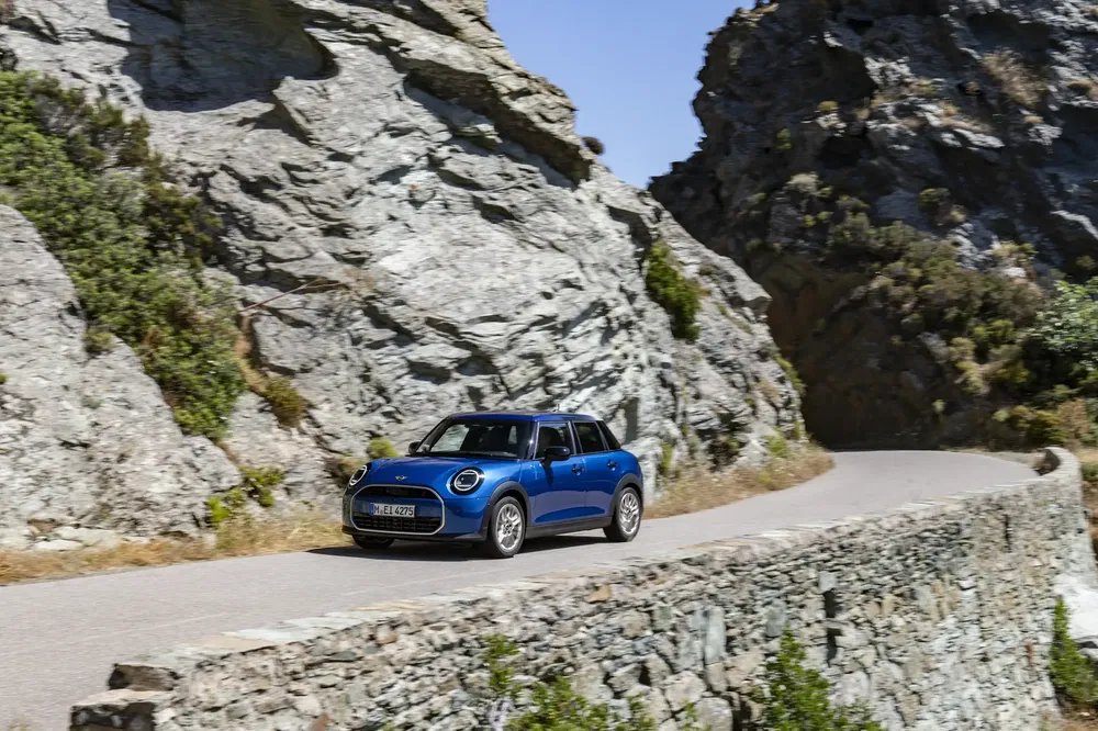 Mini Cooper bleue roulant sur une route sinueuse entre des formations rocheuses.