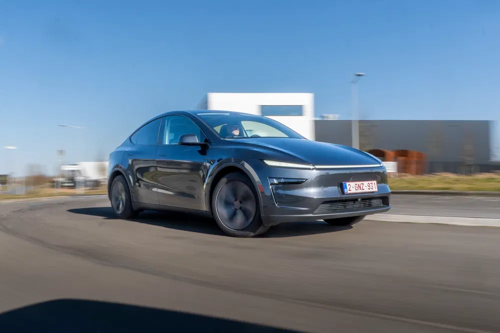 Futuristische elektrische auto in beweging op een lege weg onder een heldere blauwe lucht.