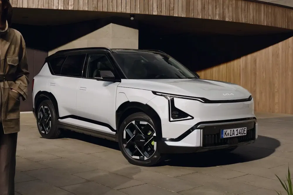 SUV Kia blanc moderne garé devant un bâtiment en bois.
