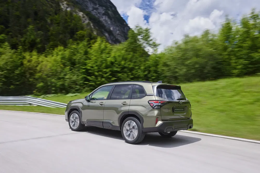 Groene Subaru Forester op een schilderachtige bergweg, gedeeltelijk bewolkte hemel.