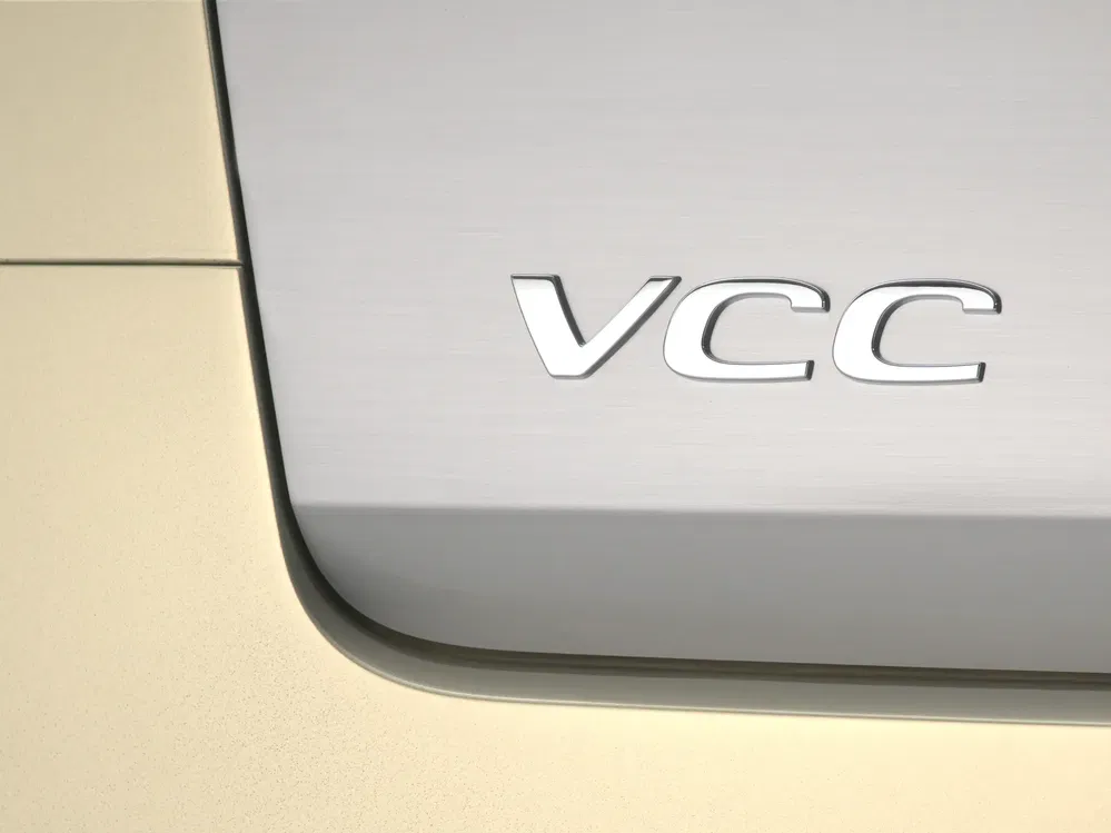 Close-up van een VCC-logoplaatje op een metalen oppervlak van een auto.