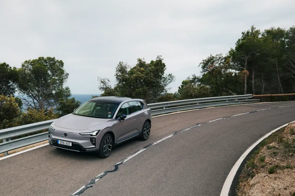 Voiture électrique moderne grise sur route sinueuse avec arbres, vue dans un environnement naturel.