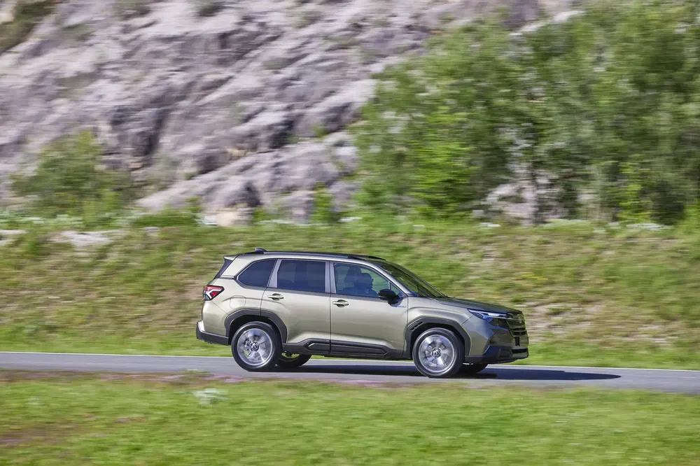 Subaru Forester SUV rijdt op landweg, berglandschap op de achtergrond.