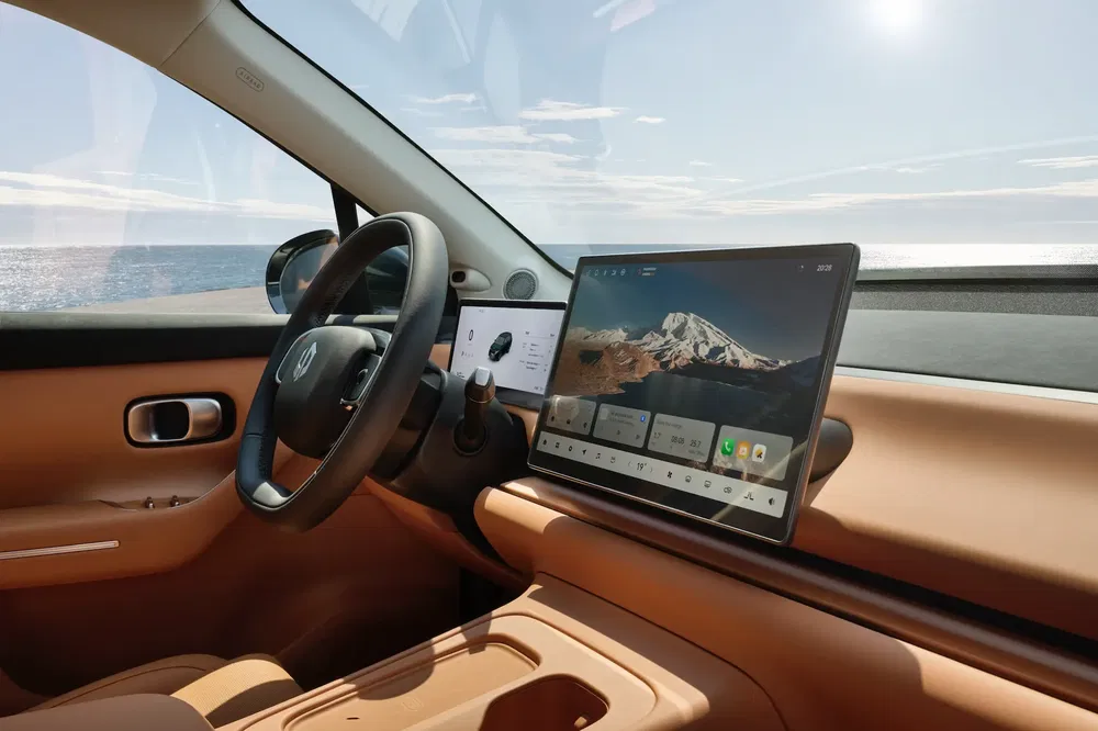 Interieur van een moderne elektrische Renault met groot touchscreen, zeezicht op de achtergrond.
