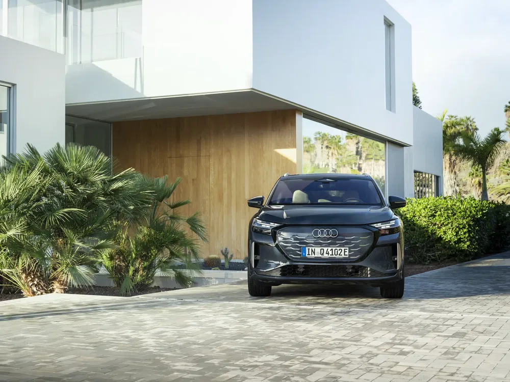 Audi Q4 e-tron noir garée devant une maison moderne avec palmiers et allée pavée.