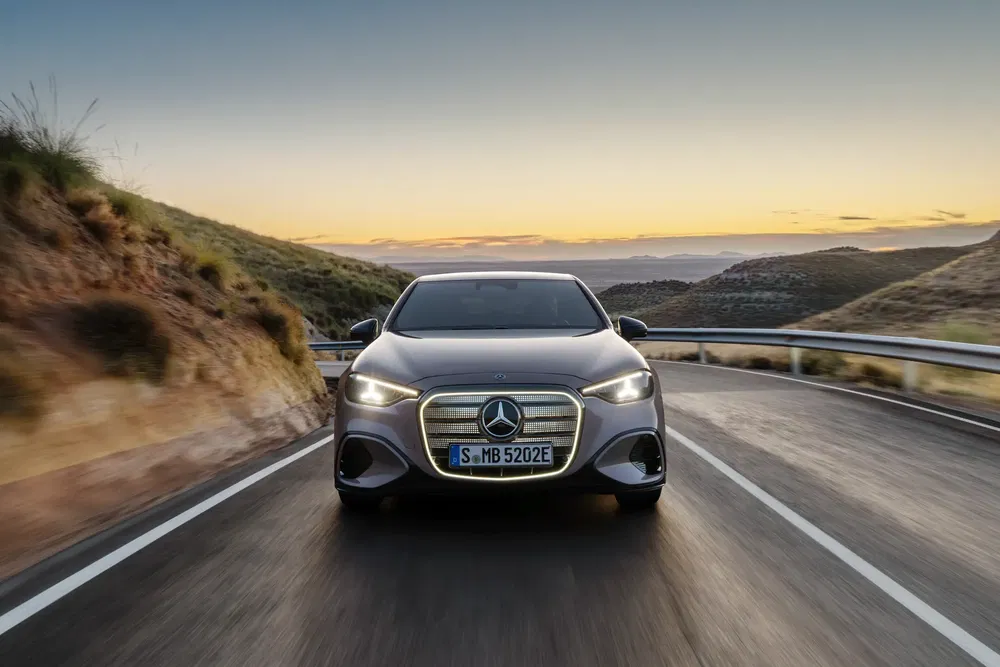 Mercedes-Benz sur route sinueuse au coucher du soleil, montrant sa calandre emblématique.