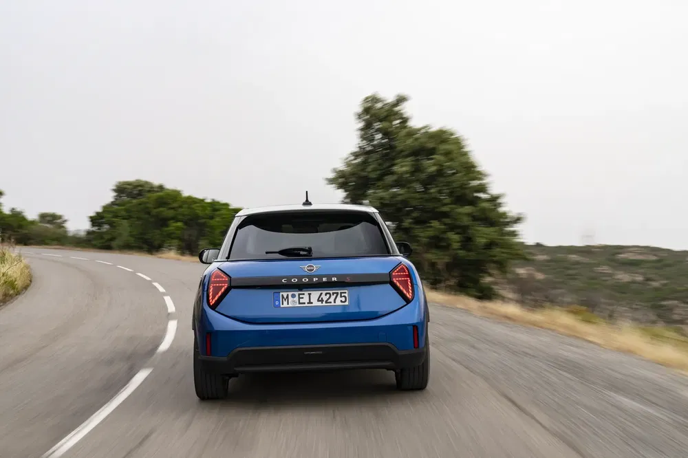 MINI Cooper S bleu roulant sur une route sinueuse entourée de verdure.