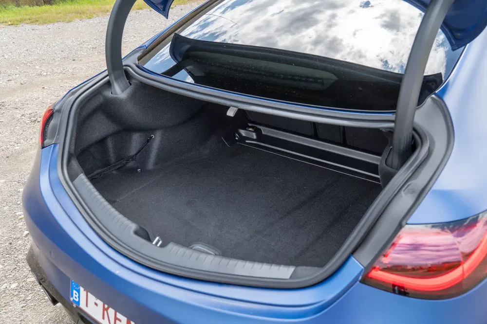 Coffre spacieux d'une BMW Série 3, couleur bleue, ouvert sur un fond de gravier.