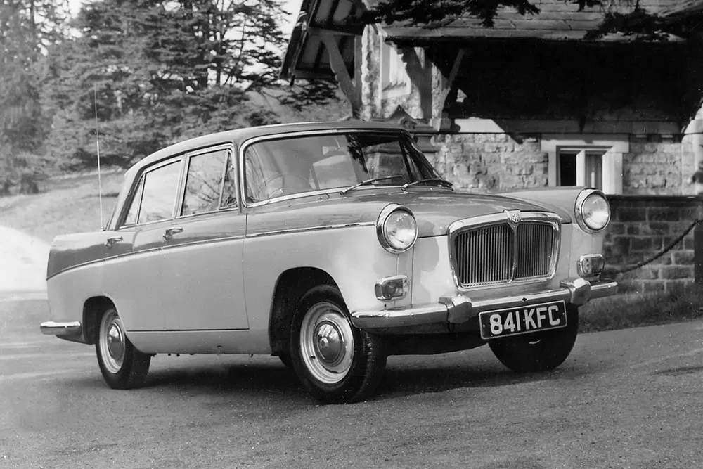 Voiture classique MG, probablement des années 1960, stationnée devant une maison en pierre.