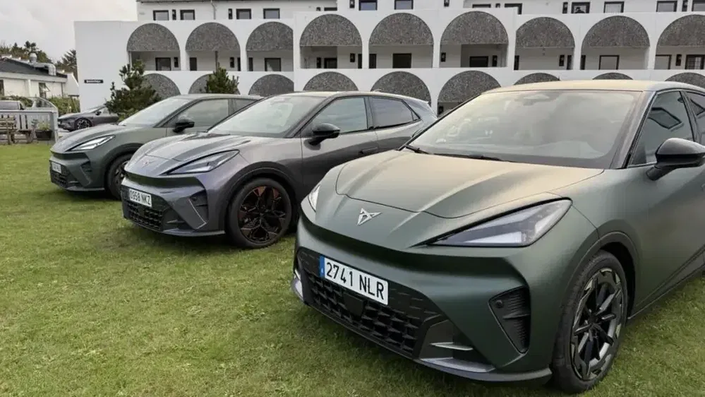 Trois Cupra Born alignées sur l'herbe devant un bâtiment moderne à arcs.
