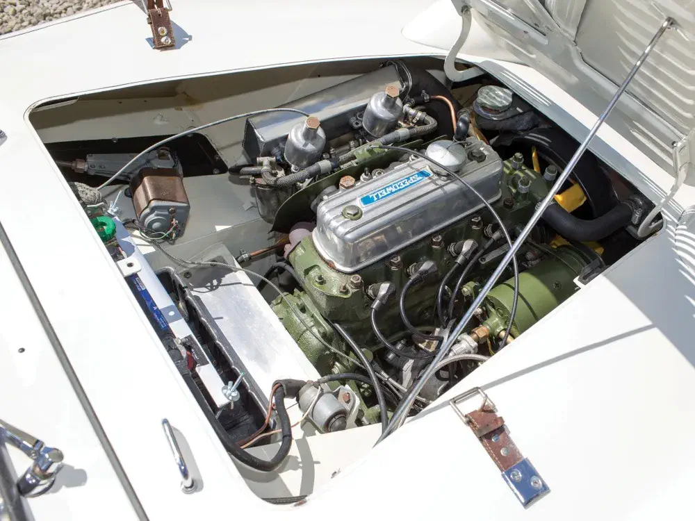 Moteur Triumph classique exposé dans le capot d'une voiture vintage, composants visibles et détails clairs.