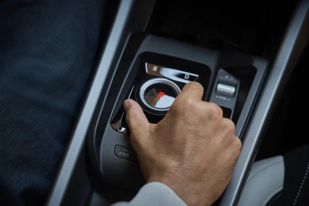 Hand stelt draaiknop van moderne auto-versnellingspook in, wijzerplaat toont P in rood.