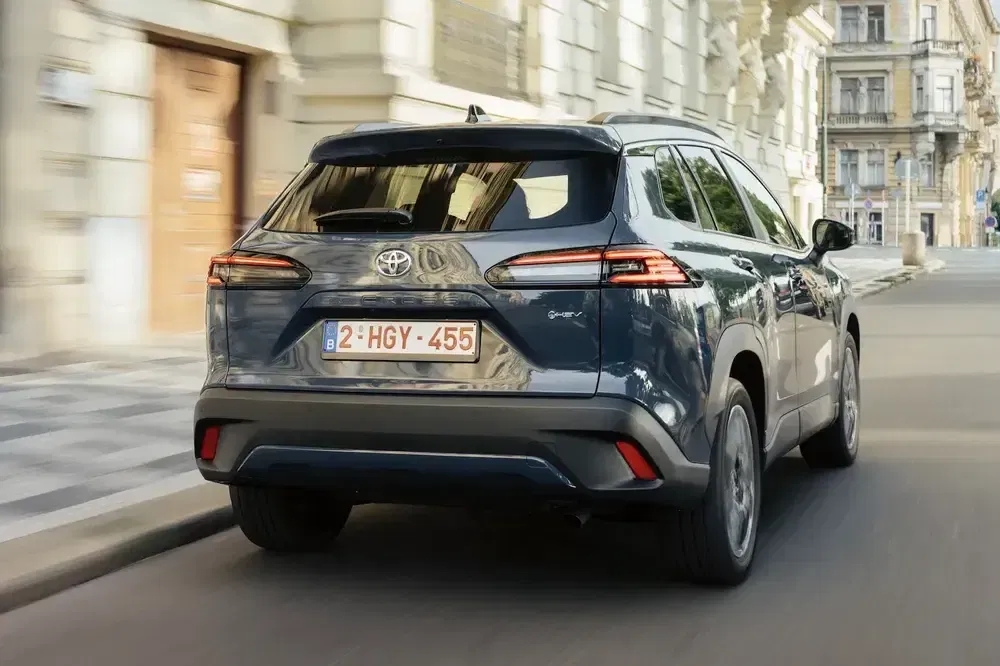 Blauwe Toyota Corolla Cross rijdt door een historische stedelijke straat met oude gebouwen.